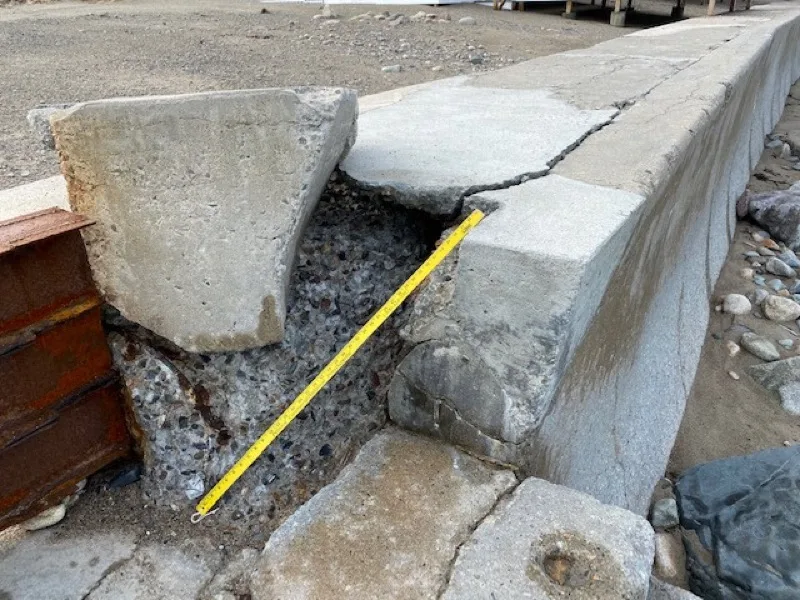 Broken concrete cap on the seawall with a tape measure showing the void beneath