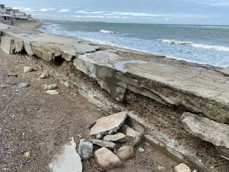 Collapsed seawall slabs along the Scituate shoreline with homes in the background